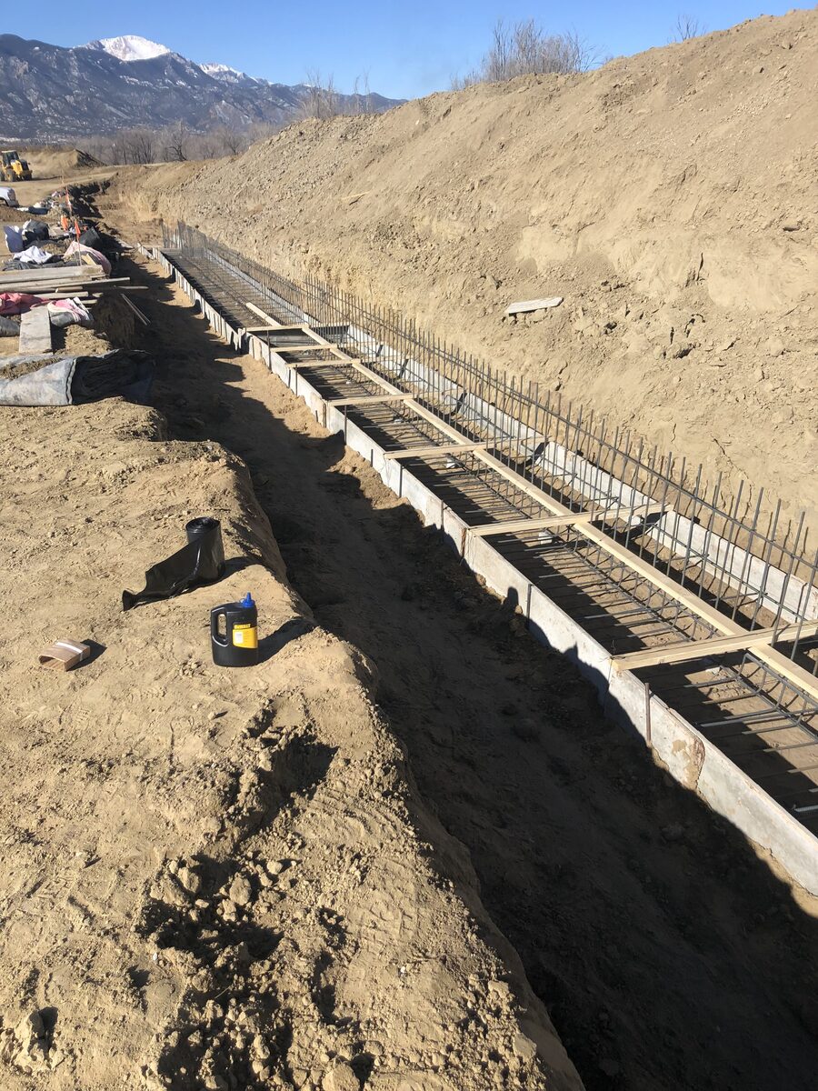 Concrete footing formwork and tied rebar in an excavated trench with Pikes Peak in the distance