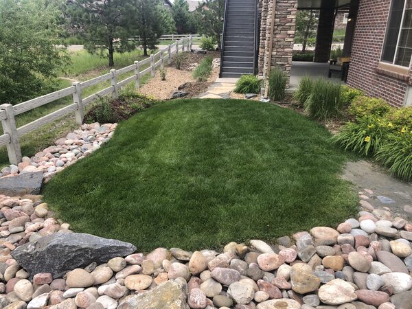 Existing turf mound with river rock border and split rail fence before renovation