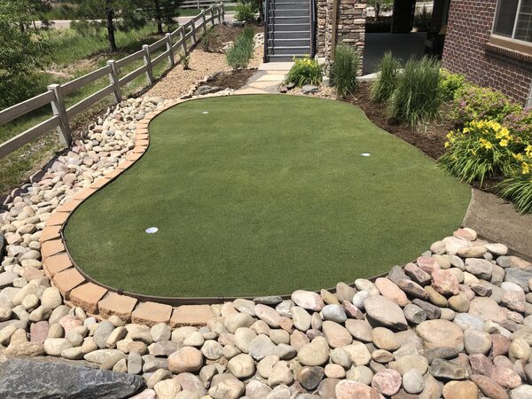 Finished artificial turf putting green with two cups, paver edging and river rock surround