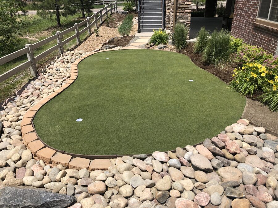 Artificial turf putting green installed by Metropolitan Total Property in a Colorado residential backyard, edged in paver brick and river rock