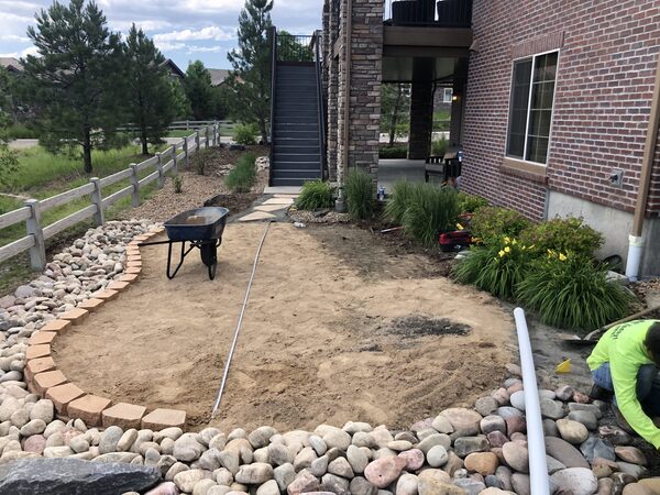 Base preparation underway with wheelbarrow, brick paver edging and irrigation line visible